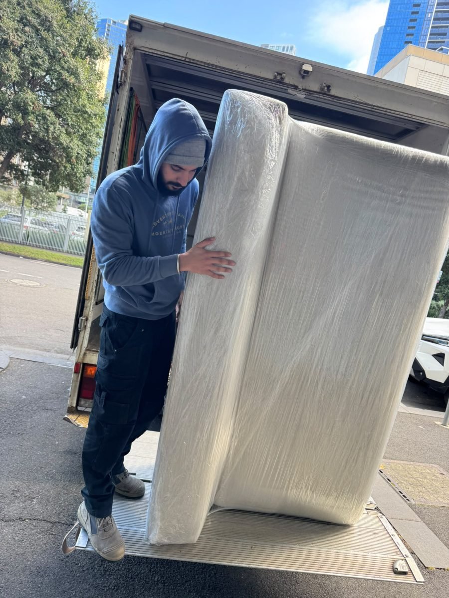 Sam's Removals crew member loading a shrink-wrapped sofa on the truck tail lift
